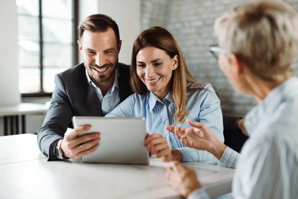 Happy couple using touchpad while having a meeting with their insurance agent in the office